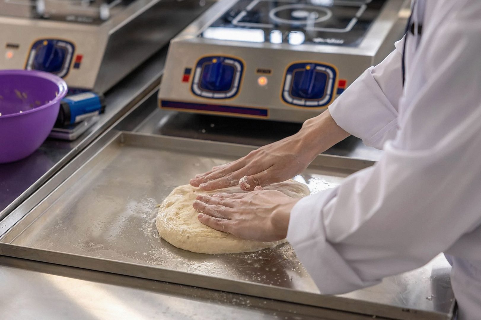 A chef is kneading dough on a stainless steel counter in a commercial kitchen.